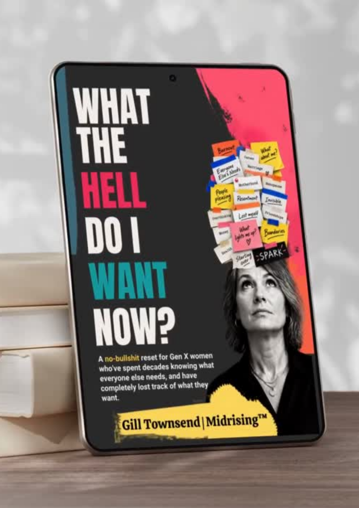 A tablet device displaying the book cover of 'What The Hell Do I Want Now?' by Gill Townsend, styled on a wooden surface with stacked books in the background.